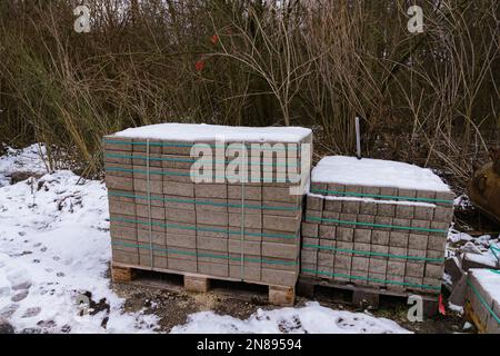 Zwei Holzpaletten mit Straßenfliesen auf einer schneebedeckten Baustelle. Stockfoto