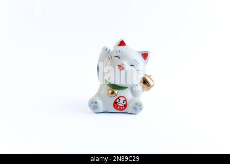 Ein Maneki-Neko oder auch bekannt als Glückskatze in Porzellan. Symbolisiert Glück und Reichtum, auf einem weißen, isolierten Hintergrund. Stockfoto