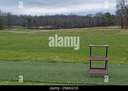 Die leere Driving Range ist für die Saison auf einem Golfplatz mit Bällen, die auf dem Gras verstreut sind, mit weiter entfernten Markierungen und einem Taschenhalter im Vordergrund geschlossen Stockfoto