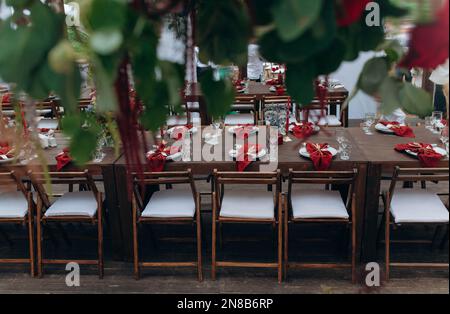 Hochzeit im Freien. Lange Banketttische, auf den Tischen sind Blumenarrangements, Kerzen, Teller mit Servietten, Gläser und Besteck im Herbststil Stockfoto