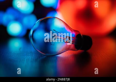 Eine selektive Fokusaufnahme einer Glasbirne auf blauem rotem Bokeh-Hintergrund Stockfoto