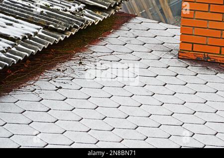 Der Rand von zwei Dächern mit verschiedenen Beschichtungen, die mit frischem Schnee bedeckt sind. Selektiver Fokus Stockfoto