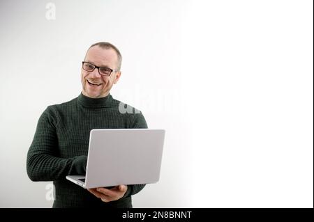 Ein Mann mittleren Alters, der mit einer Brille kahl und mit einem Laptop Spaß hat. Er zeigt anderen seine Gefühle. Er ist Professor in einem dunkelgrünen Golf. Er strahlt Freuden für Schüler aus. Eine Vorlesung für Vorträge mit einem Laptop Stockfoto