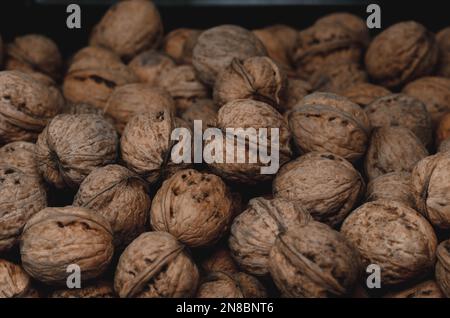 Walnuss-Hintergrund Nahaufnahme. Nicht ausgelöste, getrocknete Samen des Walnussbaums Juglans regia. Ein Haufen ganzer Nüsse mit Schalen, die als Snack zum Backen verwendet werden Stockfoto