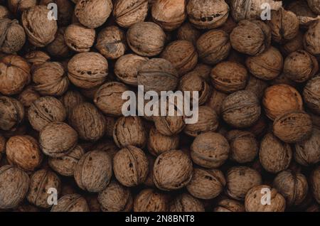 Walnuss-Hintergrund Nahaufnahme. Nicht ausgelöste, getrocknete Samen des Walnussbaums Juglans regia. Ein Haufen ganzer Nüsse mit Schalen, die als Snack zum Backen verwendet werden Stockfoto