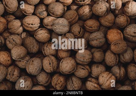 Walnuss-Hintergrund Nahaufnahme. Nicht ausgelöste, getrocknete Samen des Walnussbaums Juglans regia. Ein Haufen ganzer Nüsse mit Schalen, die als Snack zum Backen verwendet werden Stockfoto