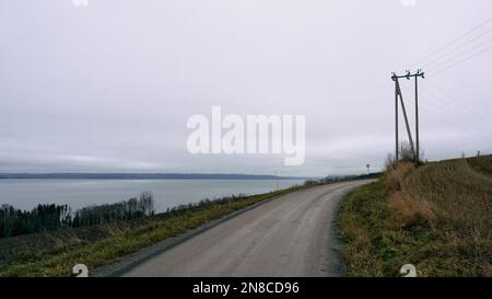 Eine wunderschöne Aufnahme einer Straße durch ein Feld in der Nähe des Lake Mjosa in Norwegen Stockfoto