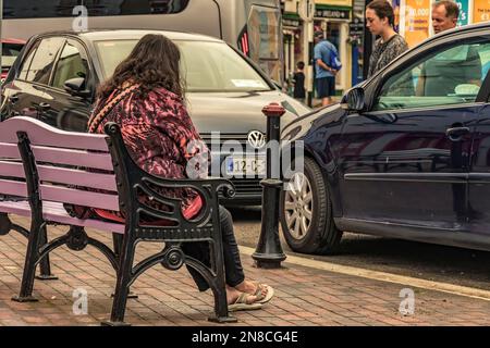Lady Heaving eine Pause, auf der öffentlichen Bank am geschäftigen Marktplatz im Stadtzentrum von Kinsale, CO Cork, Irland. Stockfoto