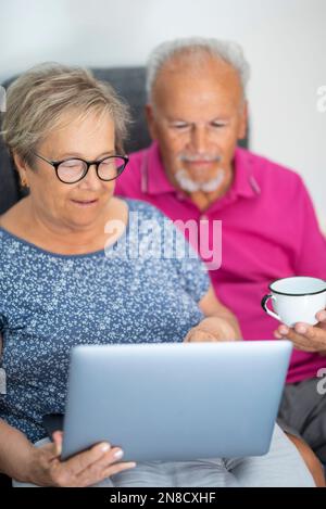Vertikales Bild einer echten älteren Lebensweise in der Freizeitaktivität in Innenräumen. Seniorenpaar, das zu Hause einen Laptop benutzt und auf dem Sofa sitzt. Moderner Mann und Frau A. Stockfoto