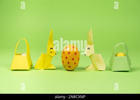 Oster-Origami - zwei Papierhasen und ein Ei mit grünem Hintergrund. Basteln für die Feiertage, machen Sie es selbst. Stockfoto
