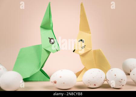 Zwei Origami-Hasen aus Papier und ein Osterei auf beigefarbenem Hintergrund. Basteln Sie Ostern mit Ihren eigenen Händen Stockfoto