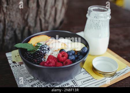 Eine Verkostung von verschiedenen frischen Früchten und verschiedenen Beeren in einer schwarzen Schüssel mit einem Glas Milch Stockfoto