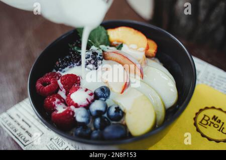 Eine Verkostung von verschiedenen frischen Früchten und verschiedenen Beeren in einer schwarzen Schüssel mit einem Glas Milch Stockfoto