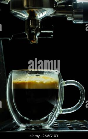 Nahaufnahme eines doppelten Espresso Shots in einer klaren Tasse, immer noch unter dem Portafilter. Stockfoto