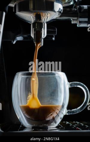 Wunderschöner karamellfarbener Espresso, der in einem klaren Glasbecher extrahiert wird. Stockfoto