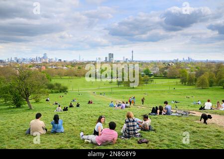 Menschen entspannen sich auf den grasbewachsenen Hängen des Primrose Hill Parks mit freiem Blick auf berühmte Gebäude auf der Londoner Skyline, North London England Stockfoto