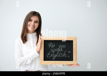 Junge Lehrerin mit Tafel und Wörtern Sprechen sie Englisch? Auf hellem Hintergrund Stockfoto