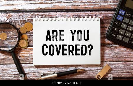 Auf einem Holztisch befindet sich ein Büroblatt mit dem Text, DEN SIE BEDECKT haben. Arbeitsplatz mit Taschenrechner, Brille, Stift, zerknittertem Papier und Stockfoto