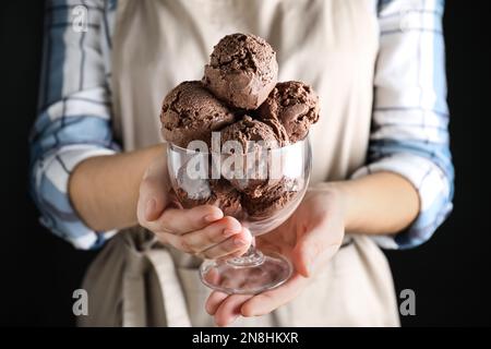 Eine Frau mit einer Glasschüssel voller Schokoladeneis auf schwarzem Hintergrund, Nahaufnahme Stockfoto
