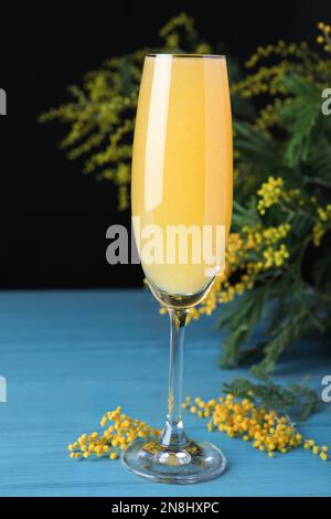 Ein Glas Mimosa-Cocktail mit blühenden Zweigen auf einem hellblauen Holztisch Stockfoto