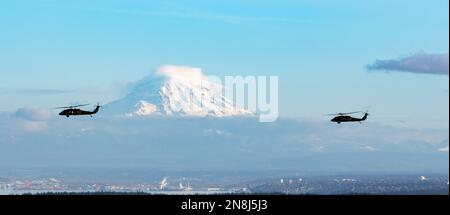 Zwei UH-60m Black Hawk Helikopter, die der Charlie Company zugewiesen wurden, 2-158 Angriffs-Helikopter-Bataillon, 16. Kampfluftfahrtbrigade fliegen am 8. Februar 2023 über Puget Sound in Washington. Mount Rainier ist im Hintergrund sichtbar. (USA Militärfoto von Kapitän Kyle Abraham, 16. Combat Aviation Brigade) Stockfoto