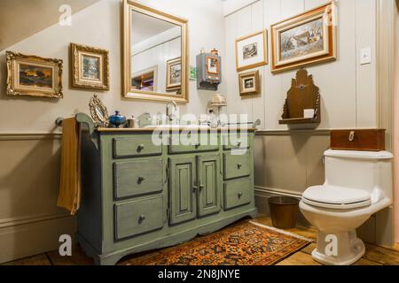 Grüner und grauer antiker Holzwaschschrank und weiße Porzellantoilette im Badezimmer auf dem Boden im alten, um 1805 Jahre alten Canadiana Cottage Haus. Stockfoto