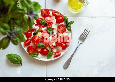 Portion Caprese-Salat unter der Basilikumpflanze, Draufsicht, Copyspace, selektiver Fokus Stockfoto