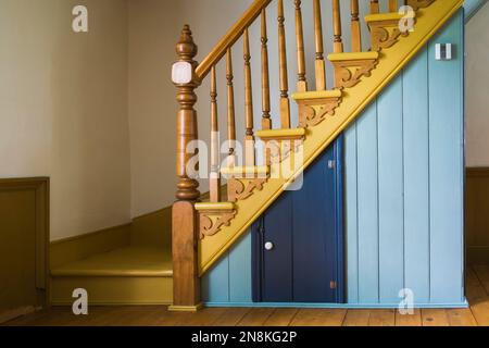 Gelb bemalte Holztreppe mit schickem Pfosten und Balustern, dekorierte Stringer im Wohnzimmer in einem alten Haus im Stil eines französischen Regimes von 1809. Stockfoto
