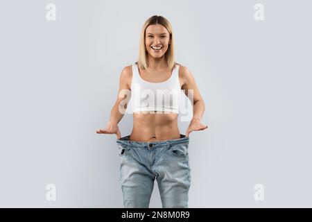 Fröhliche blonde Frau, die große Hosen trägt und lächelt Stockfoto