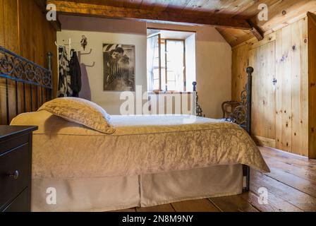 Doppelbett mit antikem schmiedeeisernem Kopfteil und Fußbrett im Hauptschlafzimmer oben in einem alten Haus um 1760. Stockfoto