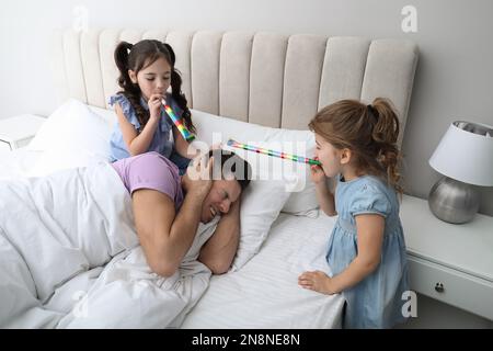 Süße kleine Kinder mit Partylöchern, die ihren Vater zu Hause aufwecken Stockfoto