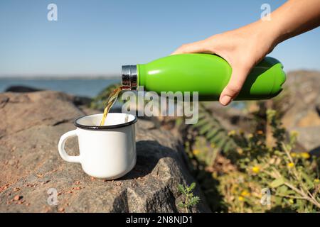 Frau, die draußen ein heißes Getränk aus der Thermosflasche in den Becher gießt, Nahaufnahme Stockfoto