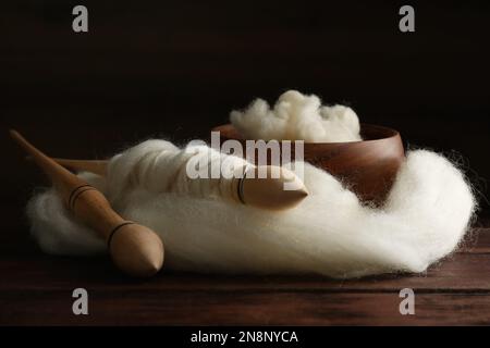 Weiche weiße Wolle und Spindeln auf Holztisch, Nahaufnahme Stockfoto