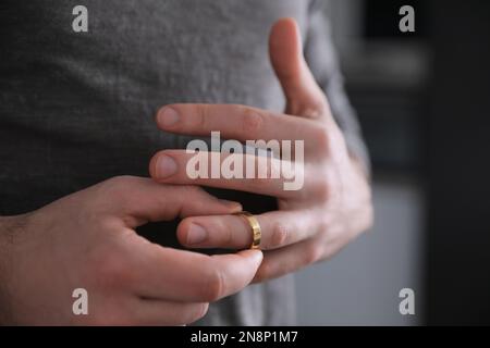 Ein Mann, der den Ehering abnimmt, auf verschwommenem Hintergrund, Nahaufnahme. Scheidungskonzept Stockfoto