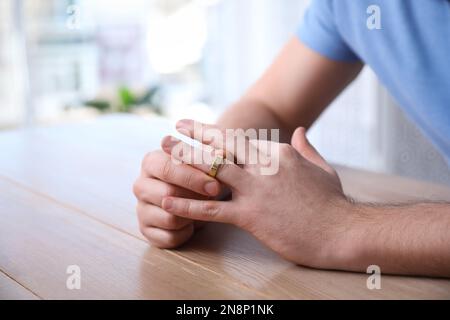 Ein Mann, der den Ehering an einem Holztisch abnimmt. Scheidungskonzept Stockfoto