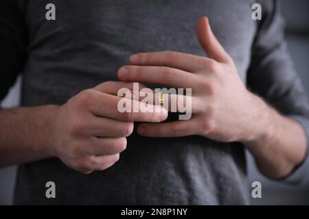 Ein Mann, der den Ehering abnimmt, auf verschwommenem Hintergrund, Nahaufnahme. Scheidungskonzept Stockfoto