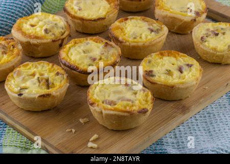 Hausgemachter Mini-Schinken und Käse-Quiches auf Holzküchen-Schneidebrett Stockfoto