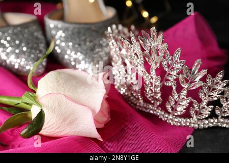 Schönes Diadem, Rose und Kleid auf dunklem Tisch, Nahaufnahme. Abschlussballkonzept Stockfoto