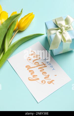 Karte mit Text HAPPY MOTHER's DAY, Geschenk und Tulpen auf mintfarbenem Hintergrund, Nahaufnahme Stockfoto