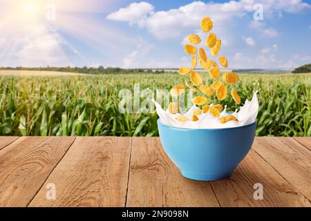 Cornflakes, die in Spritzmilch in einer blauen Schüssel mit grünem Feld auf dem Hintergrund fallen Stockfoto