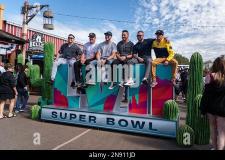 Phoenix, USA. 11. Februar 2023. American Football: Super Bowl LVII, Fanfest. Eine Gruppe von Fußballfans sitzt vor dem Super Bowl LVII auf einem Fanfestival auf dem Super Bowl Logo. Kredit: Maximilian Haupt/dpa/Alamy Live News Stockfoto