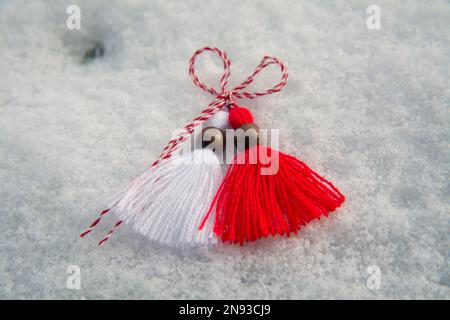 Nahtaufnahme einer rot-weißen Martenitsa (Martisol) mit Holzperlen im Schnee. Martenitsa ist ein Symbol für den bevorstehenden Frühling in Bulgarien Stockfoto