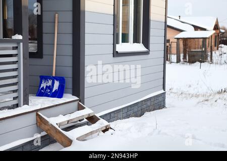 Treppe von der Veranda zum schneebedeckten Bereich. Schneeschaufel Stockfoto