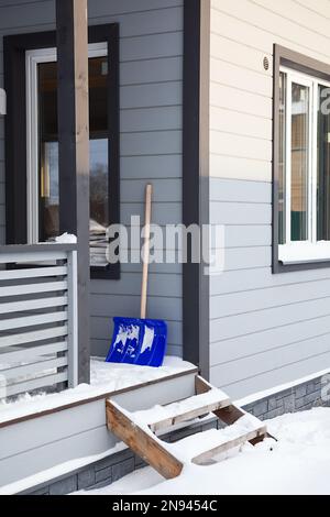 Eine Schneeschaufel lehnt sich an die Wand eines Holzhauses auf der Veranda Stockfoto