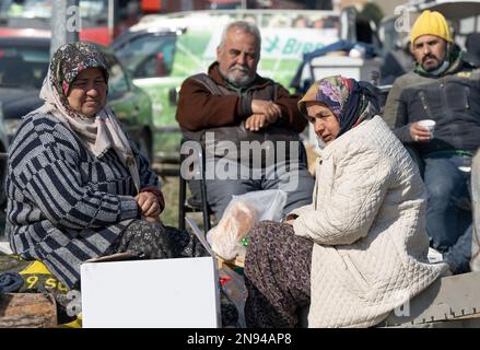 Antakya, Türkei. 11. Februar 2023. Halime Koyuncu (l) sitzt mit anderen Frauen vor einem zerstörten Haus und wartet auf die Genesung mutmaßlich verstorbener Familienmitglieder. Tausende von Opfern sollen noch immer unter den Trümmern gefangen sein. Teams von Helfern aus der ganzen Welt arbeiten im Katastrophengebiet. (Zu dpa 'Waiting for Death' aus 12.02.2023) Kredit: Boris Roessler/dpa/Alamy Live News Stockfoto