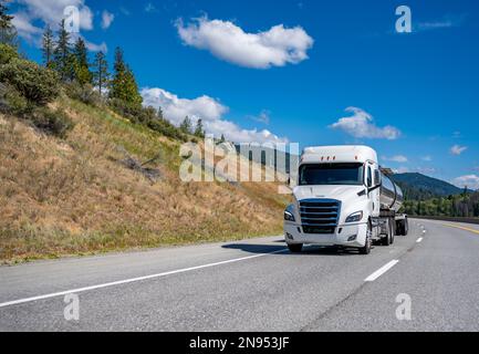 Industrieller weißer, flacher Lkw mit großer Motorhaube und Chromzubehör für den Transport von Kraftstoff in einem Tankwagen mit Auflieger auf der Berghöhe Stockfoto