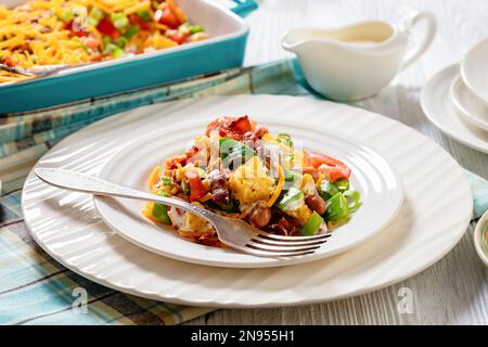 Nahaufnahme von Pinto Beans Speck Maisbrotsalat mit Tomaten, Paprika, Mais und Cheddar Käse auf einem Teller aus weißem Holz, horizontale Ansicht von oben Stockfoto