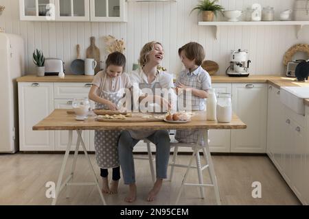 Fröhliche Mutter und zwei süße kleine Kinder mit Schürzen Stockfoto