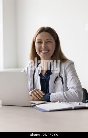 Glückliche, hübsche Ärztin, die im Krankenhaus am Arbeitstisch sitzt Stockfoto