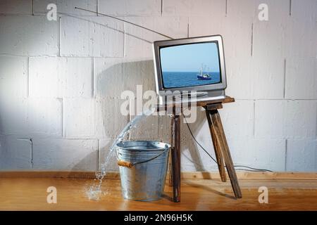 Ein alter Vintage-fernseher auf einem schrägen Holzhocker zeigt einen Film von einem Schiff auf dem Meer, aber das Wasser, das auf den Boden strömt, ohne den Eimer darunter. Gebh Stockfoto